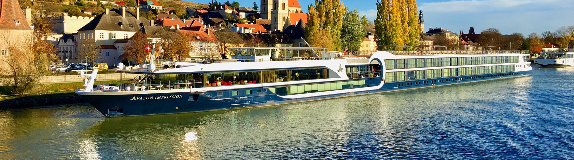 Long river cruise ship sailing past a riverside town in autumn sunshine